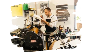 Behind the scenes at Louzape printing workshop, team member inspecting printed design on vintage press machine